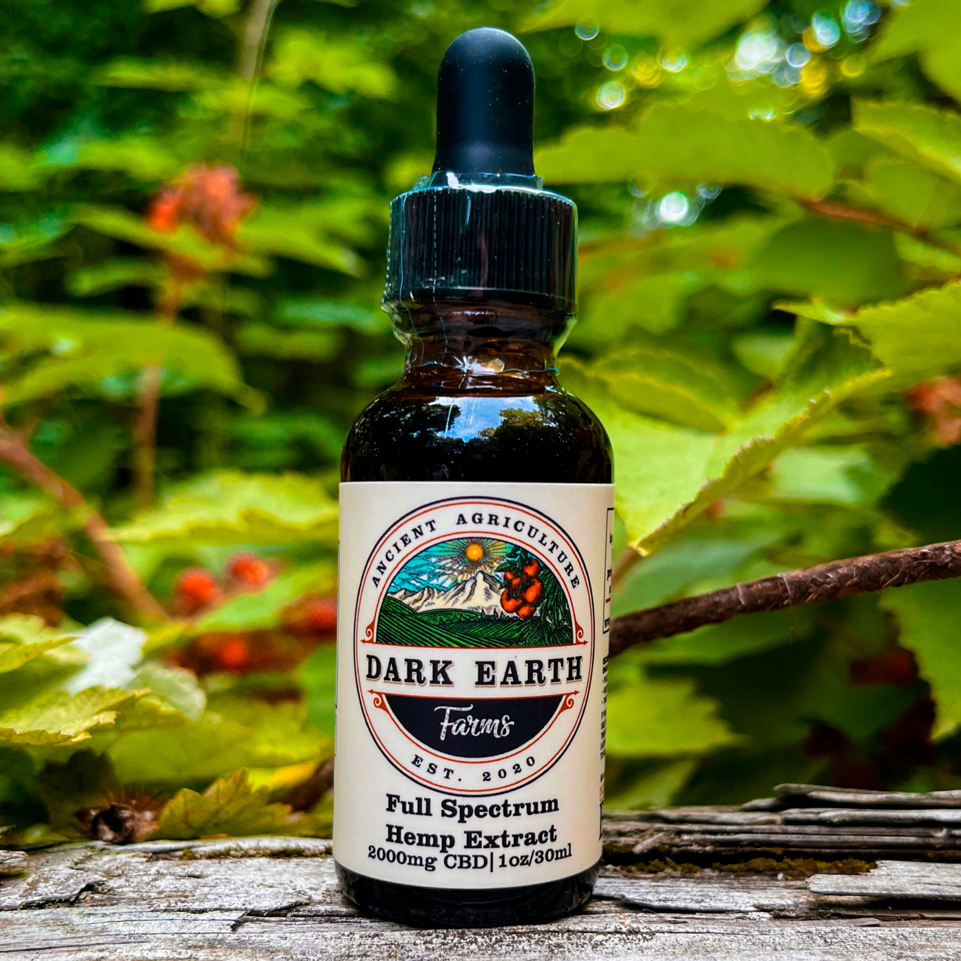 An image of a small bottle labeled Dark Earth Farms Full Spectrum Hemp Extract, featuring a green and yellow label with the brand name and product information. The bottle contains 2000mg of CBD oil with terpenes and cannabinoids, specifically designed to help alleviate pain, anxiety, and improve sleep. The bottle is placed on a wooden surface, surrounded by hemp leaves and a small dropper next to it, ready for use.